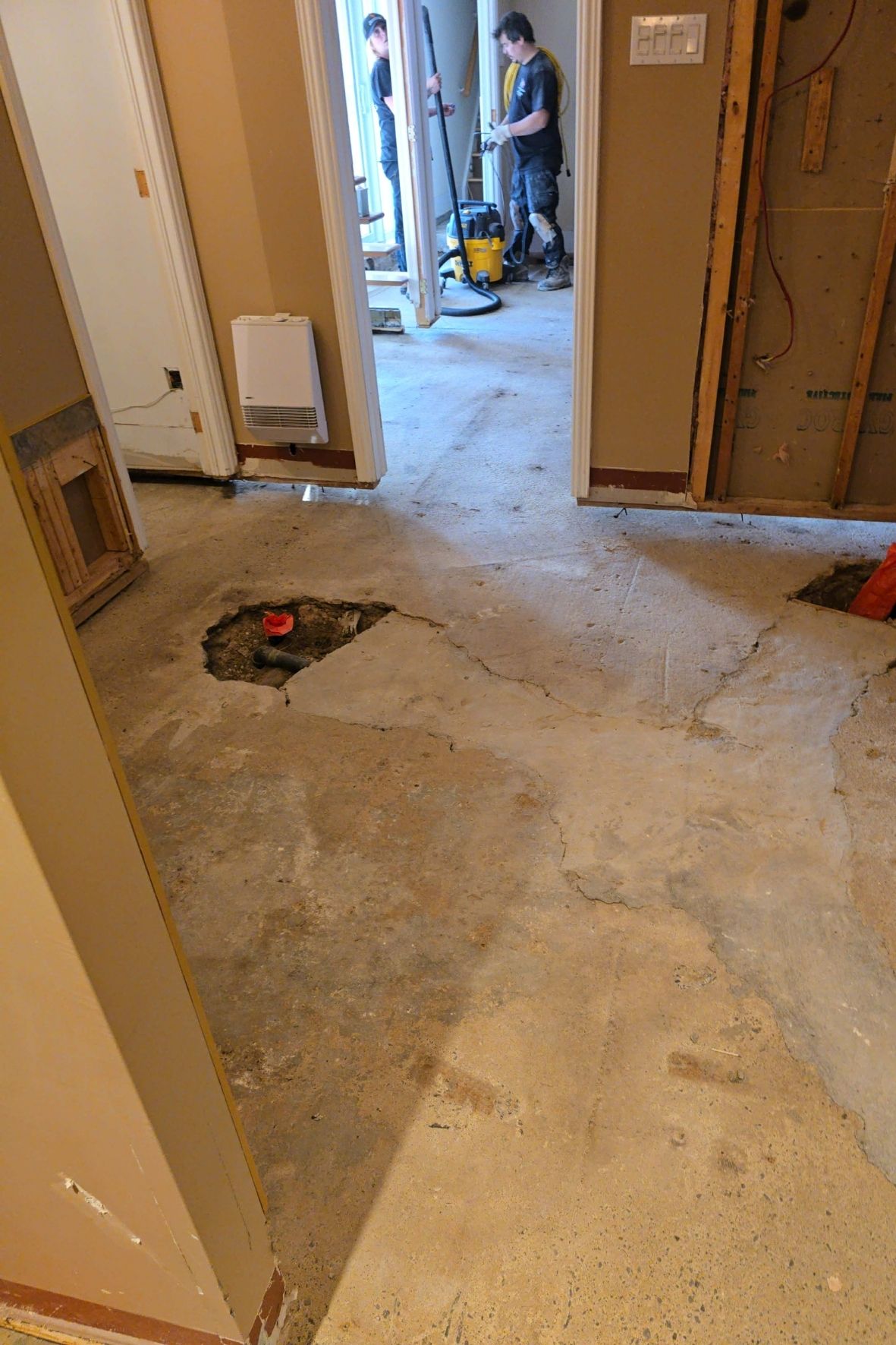 Plancher de sous-sol ouvert avec sections retirées et travailleurs en arrière-plan dans un bâtiment en rénovation  à L`Île-Bizard